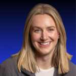 Professional woman with straight blonde hair in a grey jacket, smiling confidently before a dark blue gradient background.