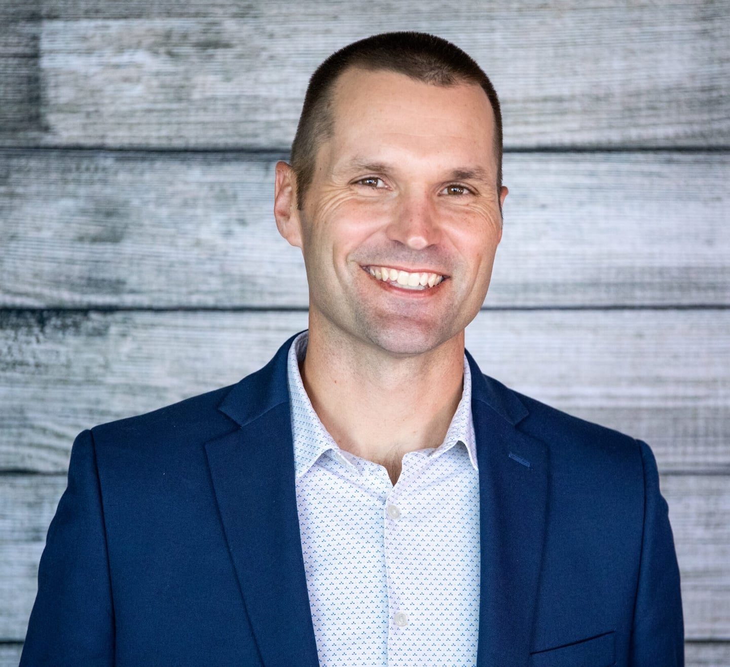 Marcus Sheridan, in a blue blazer and white patterned shirt, confidently smiles before a wooden plank background on Loqal Marketing's site.