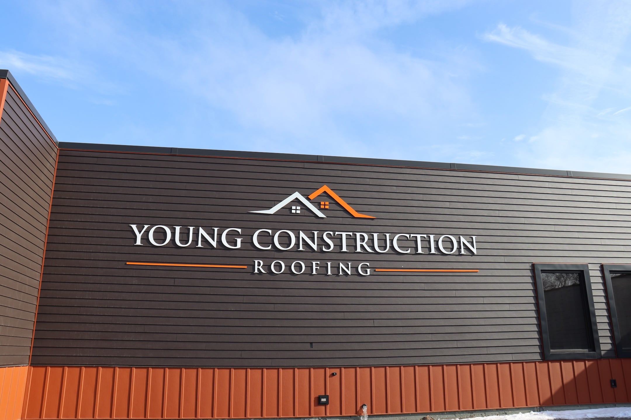 Exterior of a building with dark brown siding and orange trim featuring a prominent 