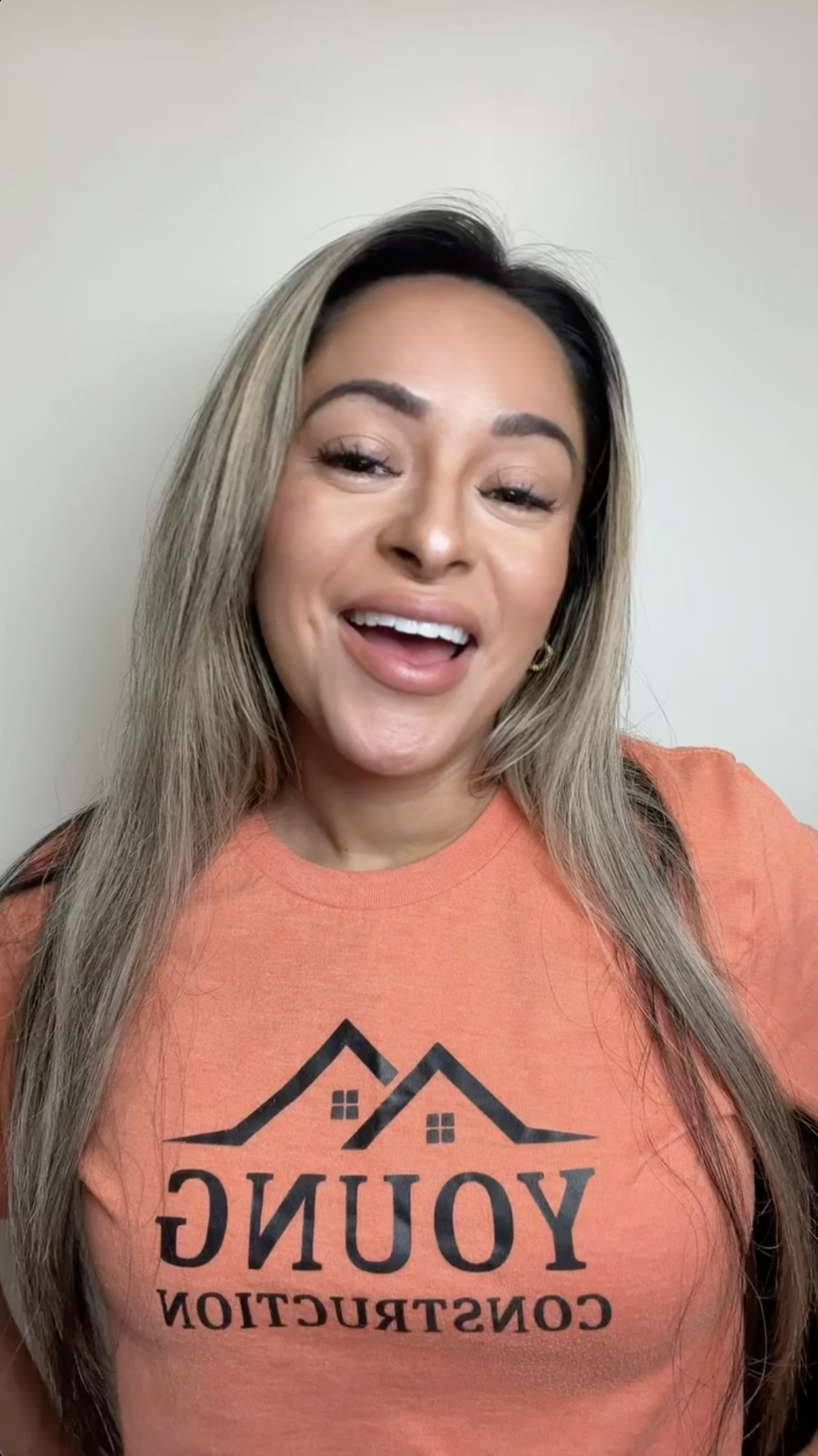 A smiling woman with long blonde hair wears an orange 